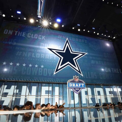 At the NFL Draft stage, the Dallas Cowboys logo stands prominently, as fans eagerly anticipate which future prospect will be selected in this pivotal round.