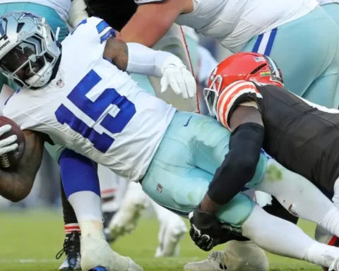 During the game, a Cowboys player in a blue and white uniform is tackled by an opponent in black and orange, showcasing intense action despite his decreasing role before the bye week.