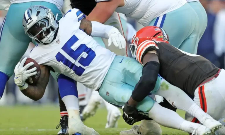 During the game, a Cowboys player in a blue and white uniform is tackled by an opponent in black and orange, showcasing intense action despite his decreasing role before the bye week.