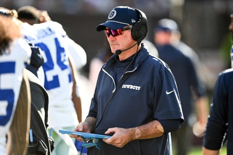 A football coach for the Cowboys, sporting sunglasses and a headset, looks at a tablet on the sidelines during a game this season.