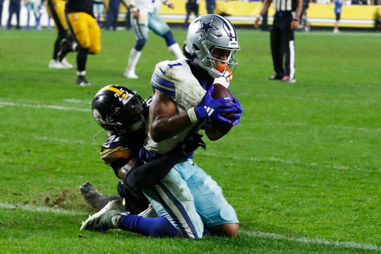 In Week 8, a Cowboys football player in white and blue uniform clutches the ball tightly while being tackled by a player in black and yellow uniform.