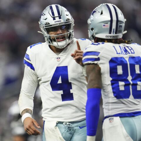 Two football players in white Dallas Cowboys uniforms, adorned with stars, communicate on the field during a game.