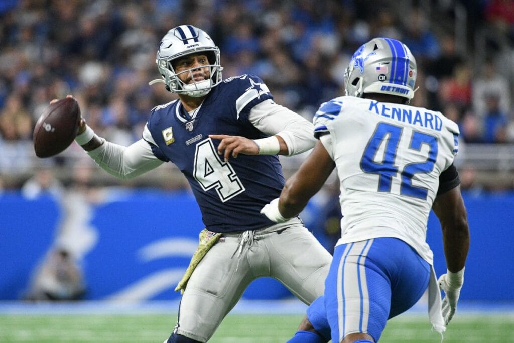 Football player in white and blue uniform throws a pass as a defender in white and blue approaches.