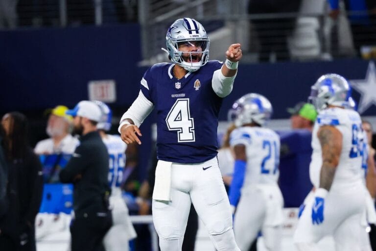 Football player in a blue uniform points forward during a game, surrounded by team members on the field.