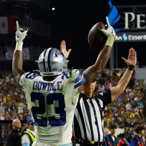 Football player celebrating a touchdown as a referee signals in a crowded stadium.