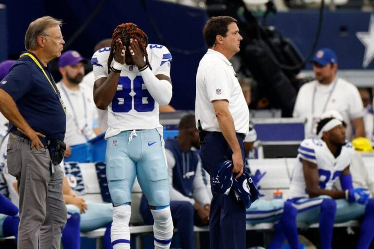 A struggling football player with head in hands on the sidelines, surrounded by coaches during a game, reflects the pressure that even Cowboys stars face amidst discussions of contract extensions.