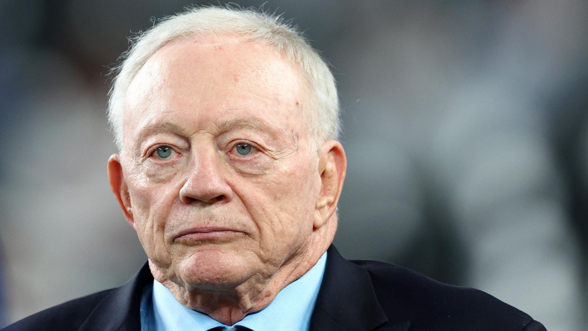 A man in a suit and tie looks ahead with a serious expression.