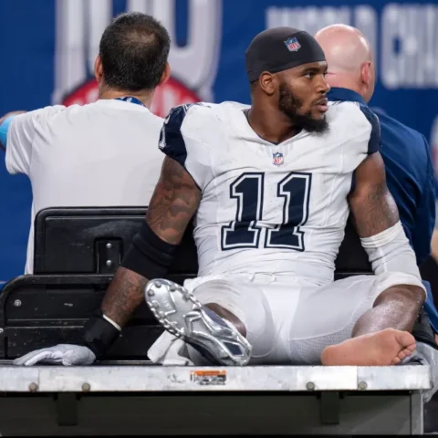 Football player in jersey number 11 being driven on a medical cart off the field.