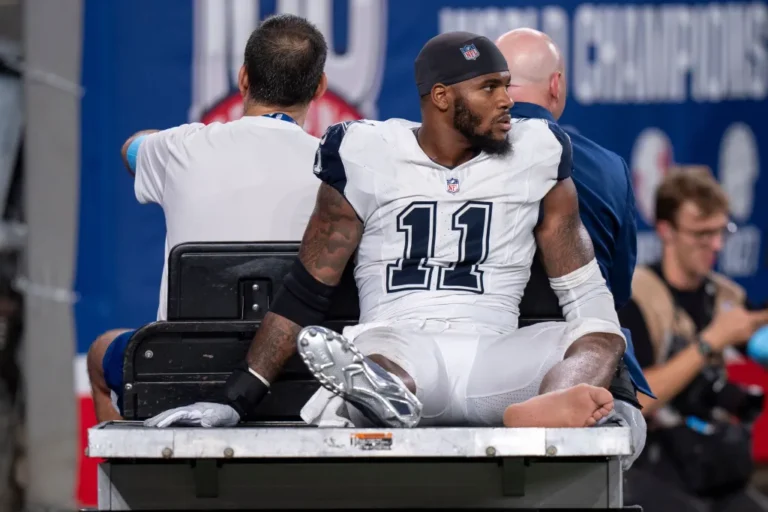 Football player in jersey number 11 being driven on a medical cart off the field.