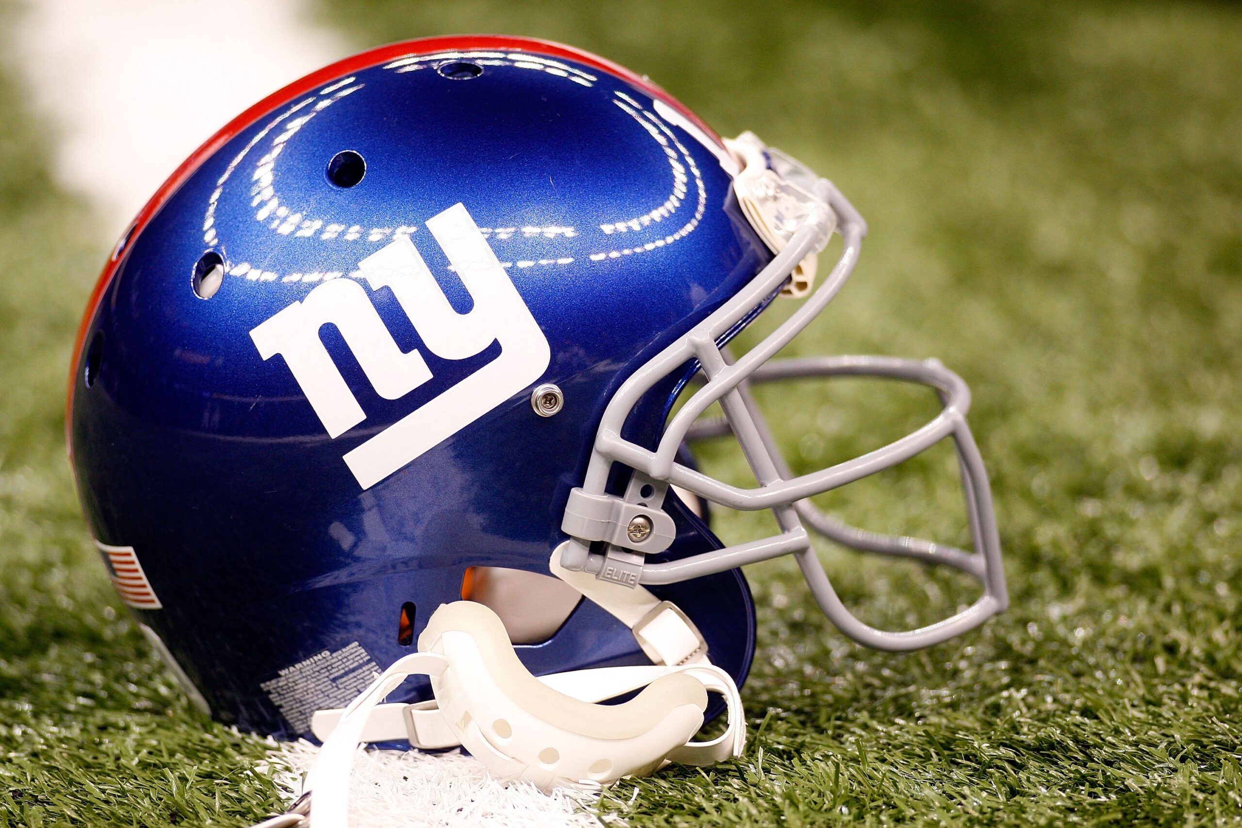 Blue football helmet with "ny" logo on green field.