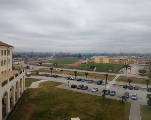 Under an overcast sky, the Dallas campus unfolds with buildings, a running track, and parked cars.