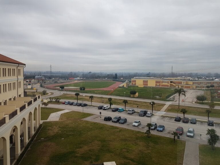 Under an overcast sky, the Dallas campus unfolds with buildings, a running track, and parked cars.