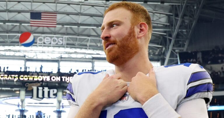 A football player with a red beard stands in a stadium, touching his collar, embodying the changing aspect of the modern-day cowboys on the field.