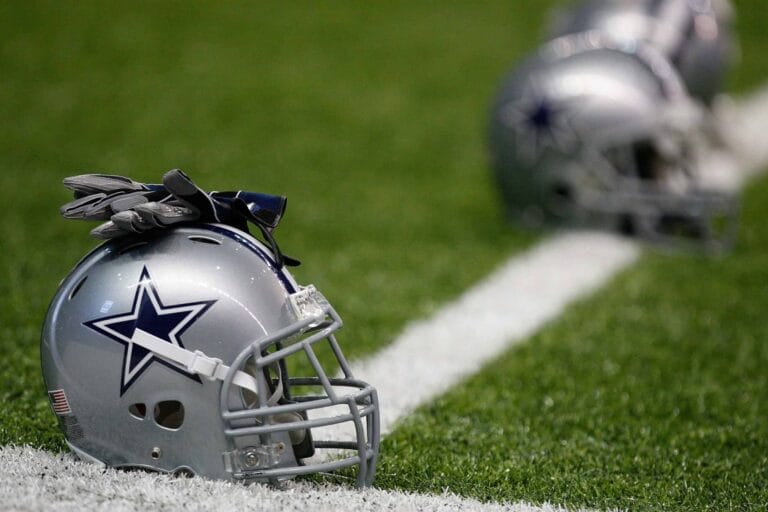 Football helmets with a star logo rested on the grass field near a white line, embodying the Cowboys spirit and beckoning players to "Play the Man.