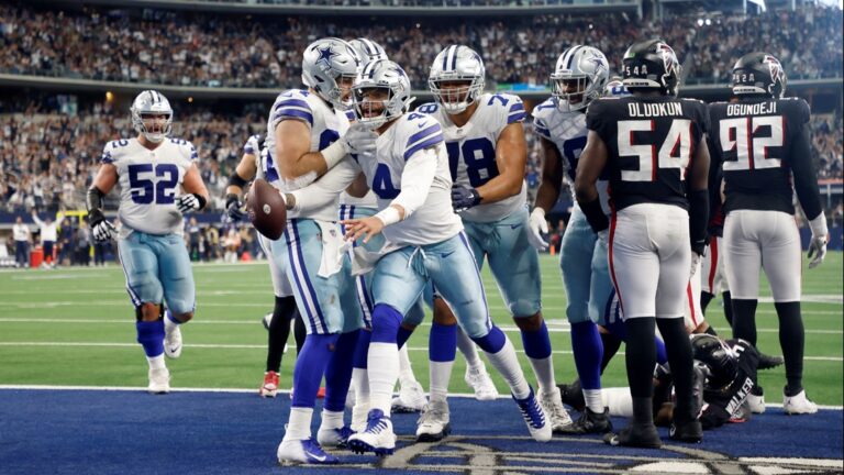 Dallas Cowboys players celebrate a touchdown on the field during Week 9, with a roaring crowd in the background.