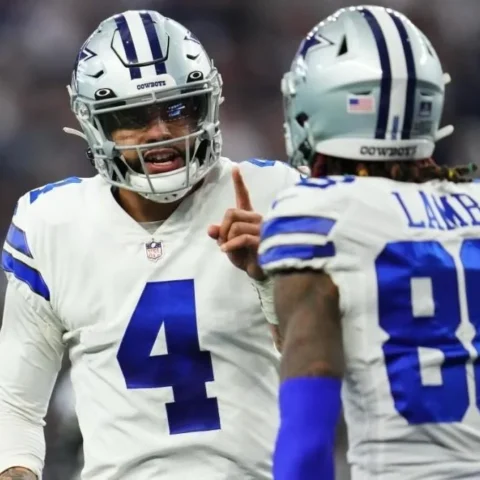 Two football players in Dallas Cowboys uniforms, with Dak Prescott leading the animated conversation, are on the field.