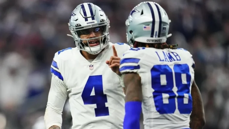 Two football players in Dallas Cowboys uniforms, with Dak Prescott leading the animated conversation, are on the field.