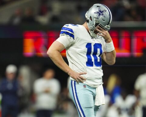 A Dallas Cowboys player stands on the field during Week 11, looking down with his hand near his face.