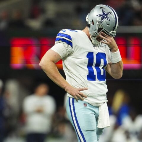 A Dallas Cowboys player stands on the field during Week 11, looking down with his hand near his face.