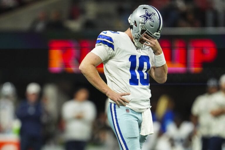 A Dallas Cowboys player stands on the field during Week 11, looking down with his hand near his face.