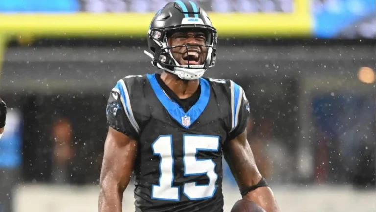 A football player in a black and blue uniform celebrates on a rainy field as rumors swirl about the Cowboys adding a wide receiver.