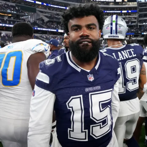 In his Dallas Cowboys uniform, the football player stands on the field, surrounded by fellow Cowboys players post-game, contemplating his future role with the team.