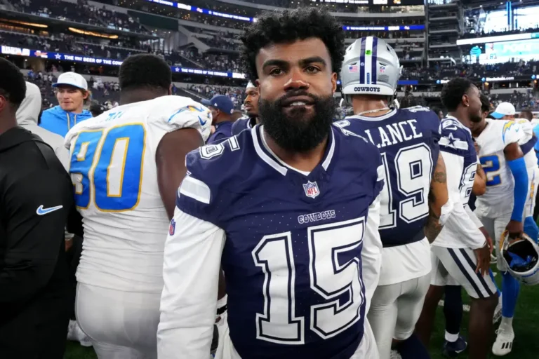 In his Dallas Cowboys uniform, the football player stands on the field, surrounded by fellow Cowboys players post-game, contemplating his future role with the team.