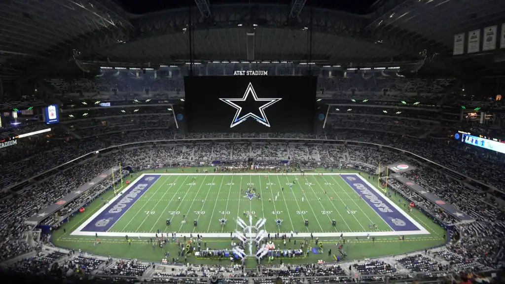Aerial view of a football field with Cowboys written in silver on the blue end zones Inside AT&T Stadium during game festivities