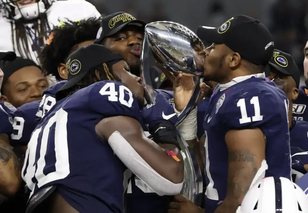Penn State players Jesse Luketa and Micah Parsons celebrating a win by kissing a trophy. Jesse Luketa and the Cowboys Superstar Connection