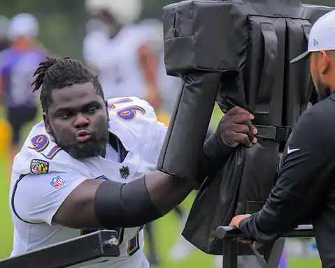 - Young football player practicing training drills with tackling dummy at practice field.